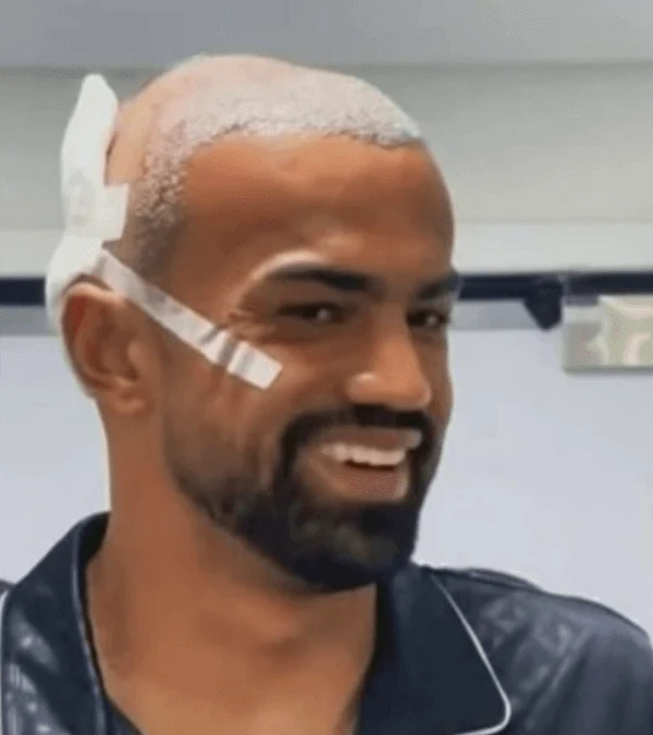 Fabrício Bruno em ambiente clínico, com cabelo raspado e curativo na lateral da cabeça.